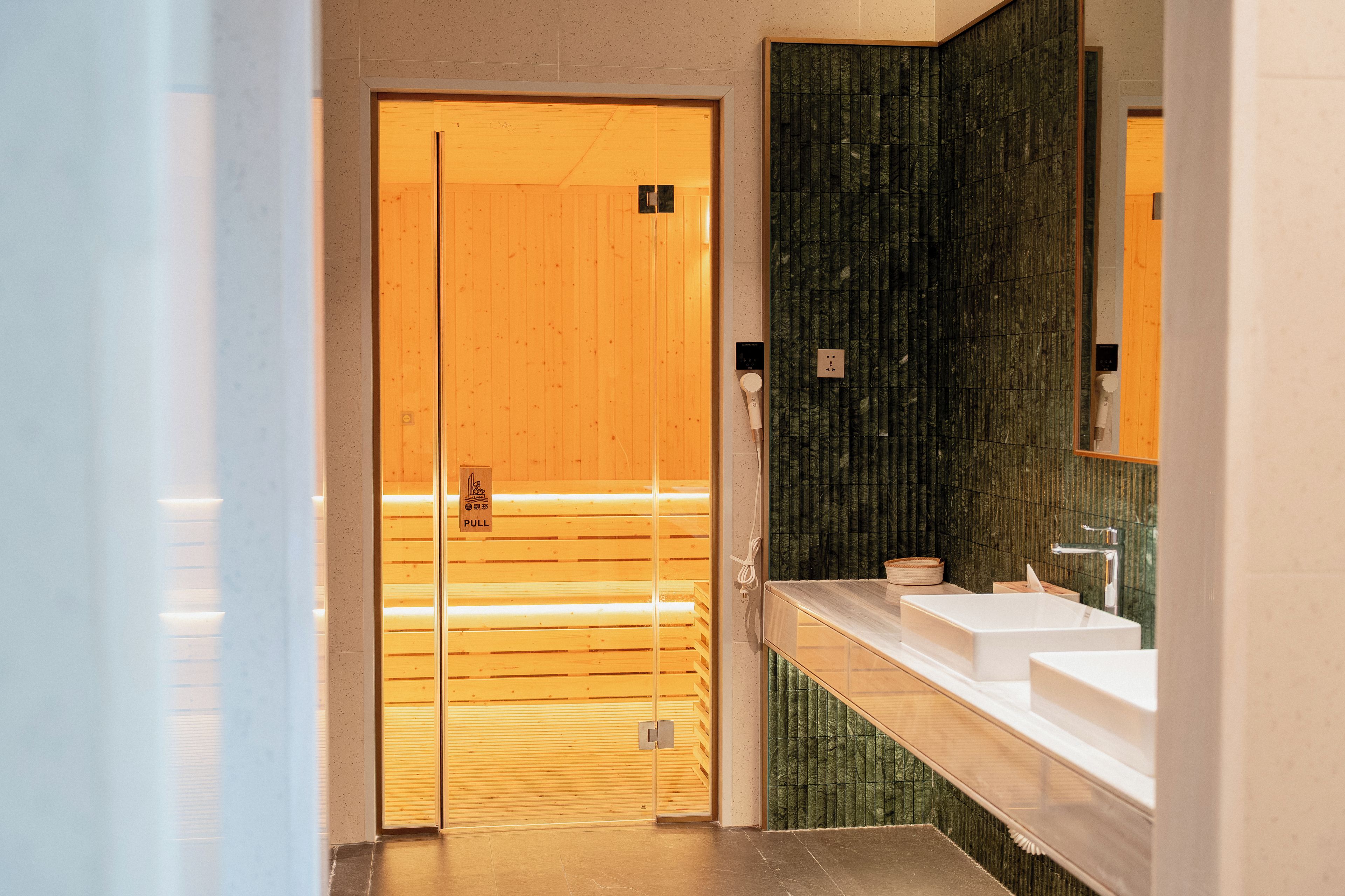 Un baño moderno con puerta de madera, un espejo grande y un lavamanos blanco.