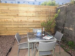Eine Terrasse im Freien mit einem Glastisch, Korbstühlen, einer Champagnerflasche und einer Zeitschrift.
