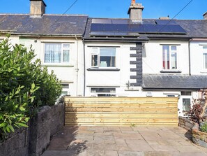 A row of terraced houses with solar panels on the roofs, a stone wall, and a wooden fence. - Angels Place (Yelverton)
