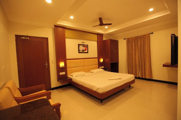 A hotel room with a bed, a chair, a ceiling fan, and a painting on the wall.