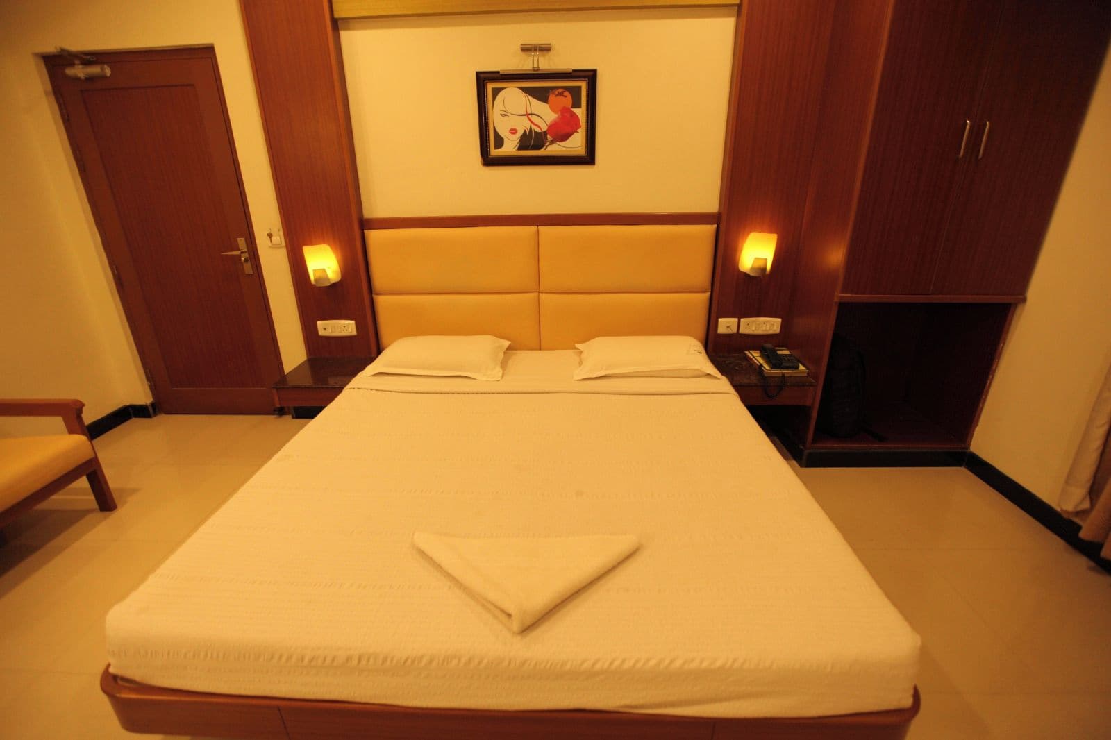 Een hotelkamer met een groot bed, nachtkastjes, een kledingkast en een lijst met een foto aan de muur.