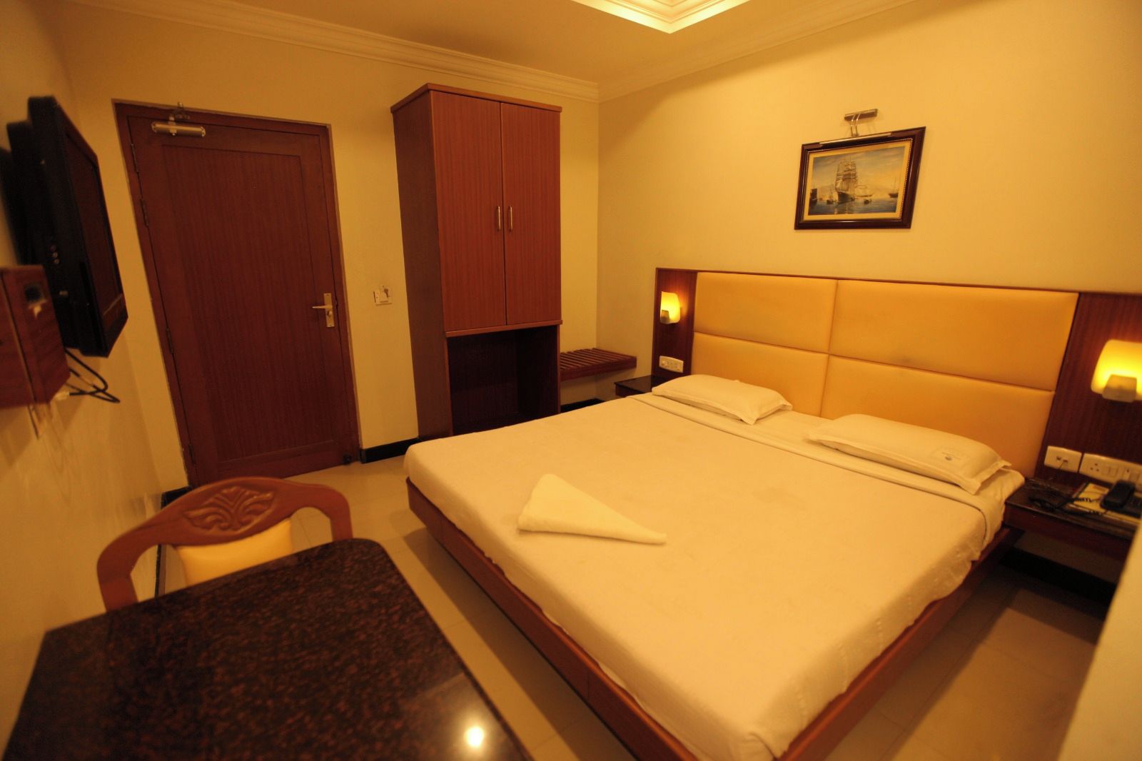 Een hotelkamer met een bed, een bureau, een stoel, een kledingkast en een schilderij aan de muur.
