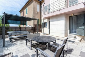 An outdoor patio with a round table and benches, a covered seating area, and a building with a garage door. - Beautiful luxury house with sea view & outside space (Split)