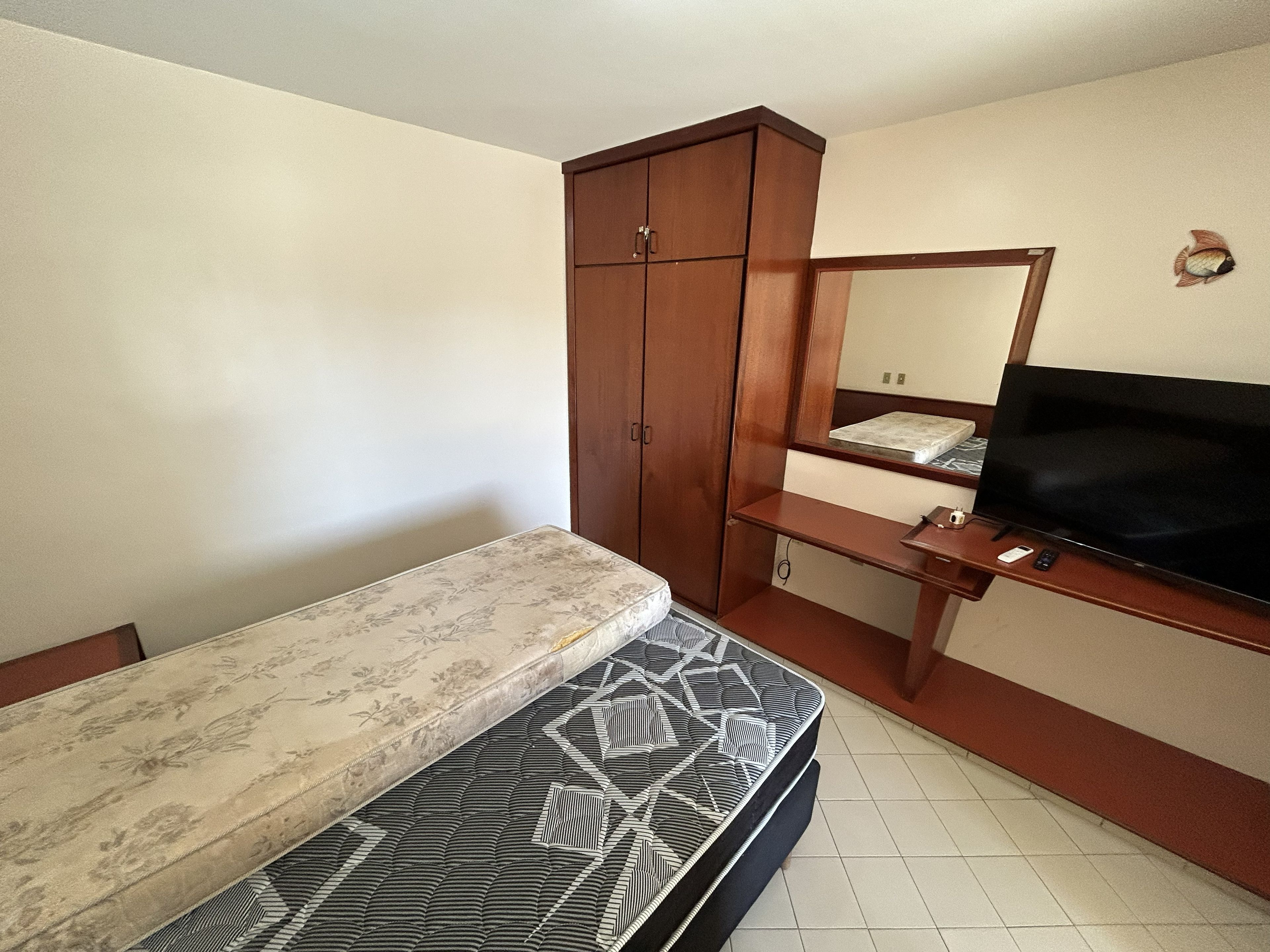 Une chambre à coucher avec un lit, une armoire en bois, une télévision et un miroir.