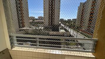 A balcony with a chain-link fence, overlooking a street with buildings and a clear sky.