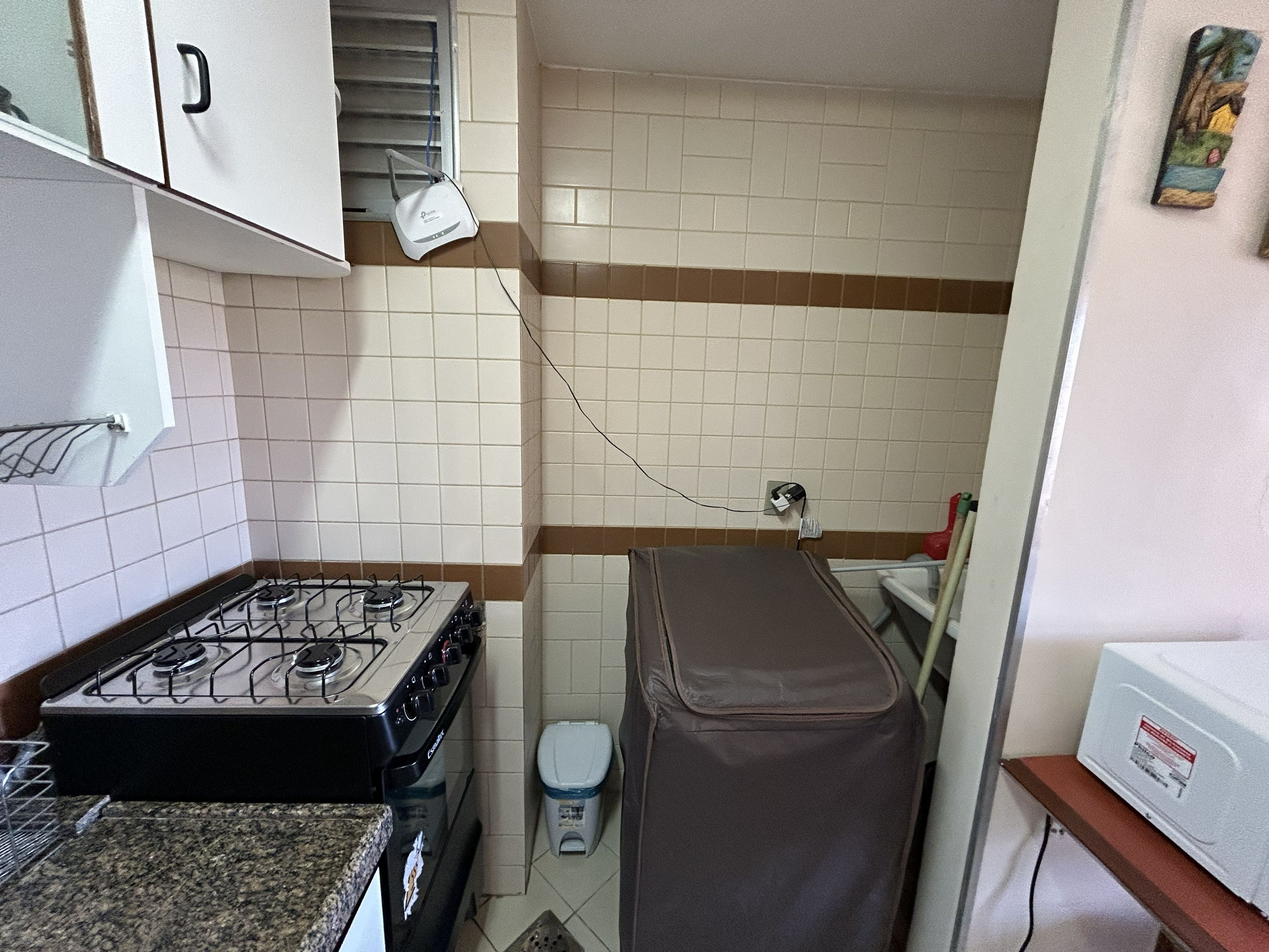 A compact kitchen with a gas stove, a trash bin, and a power outlet on the wall.