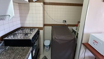 A compact kitchen with a gas stove, a trash bin, and a power outlet on the wall.