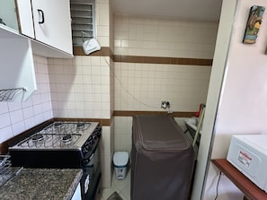 A compact kitchen with a gas stove, a trash bin, and a power outlet on the wall. - CRCN - Eldorado Flat Service (Caldas Novas)