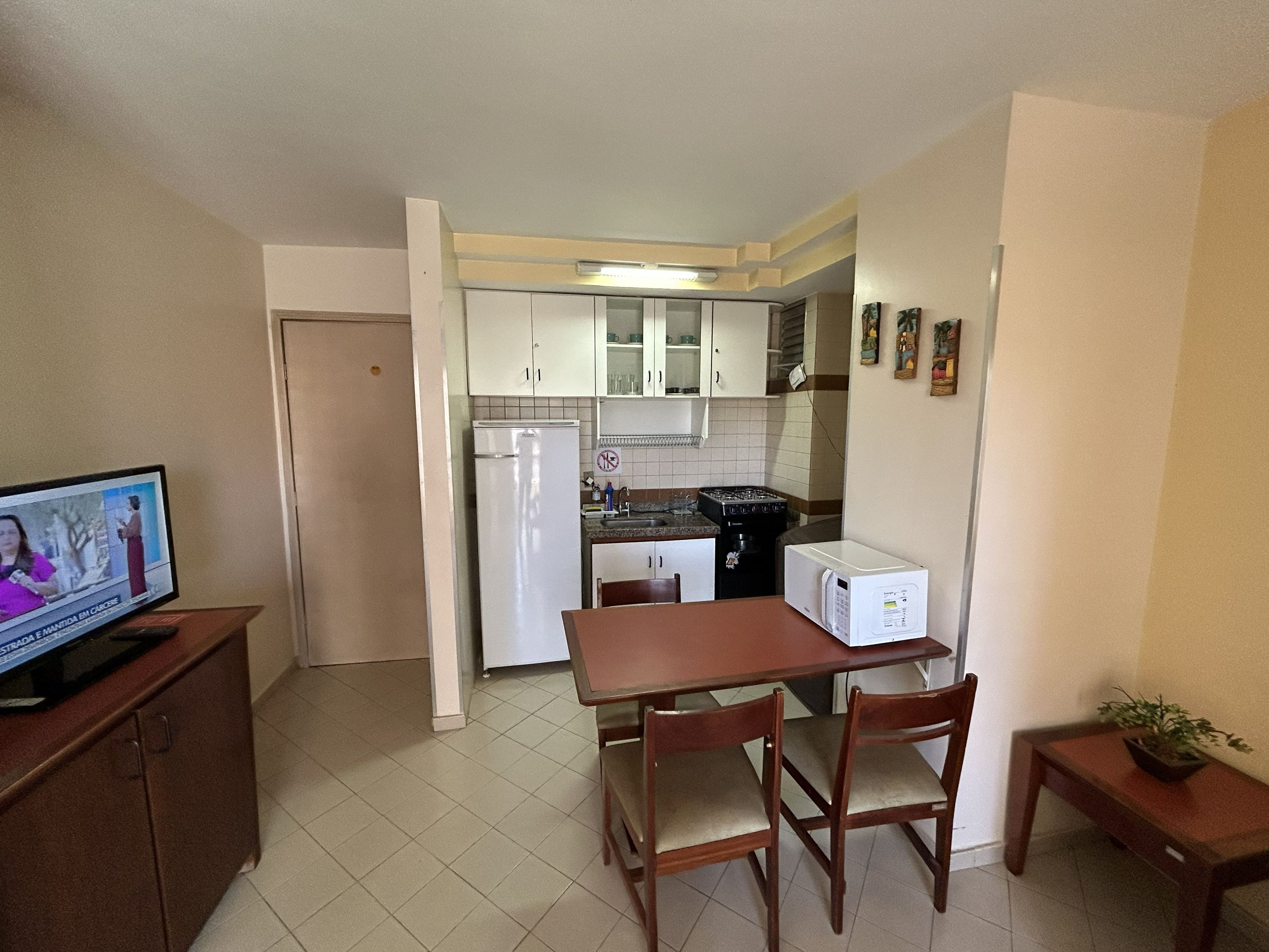 Cozinha compacta com armários brancos, geladeira, micro-ondas e área de refeições com mesa e cadeiras.