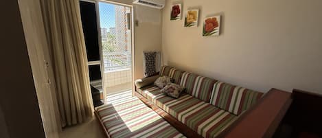 A room with a striped sofa, a small table, and a view of the outside through a sliding door.