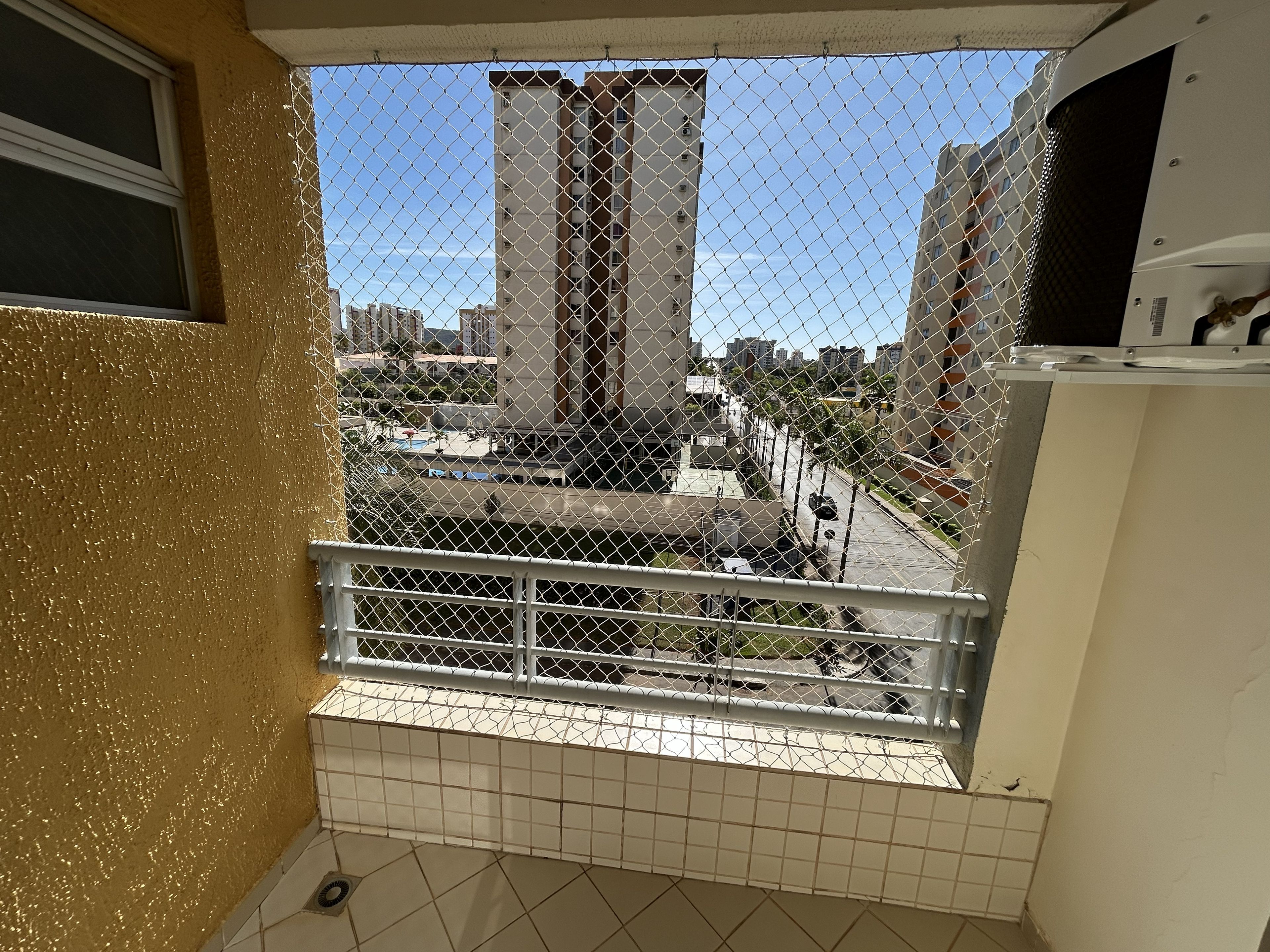 Varanda com vista para edifícios altos, chão de azulejos e cerca de arame.