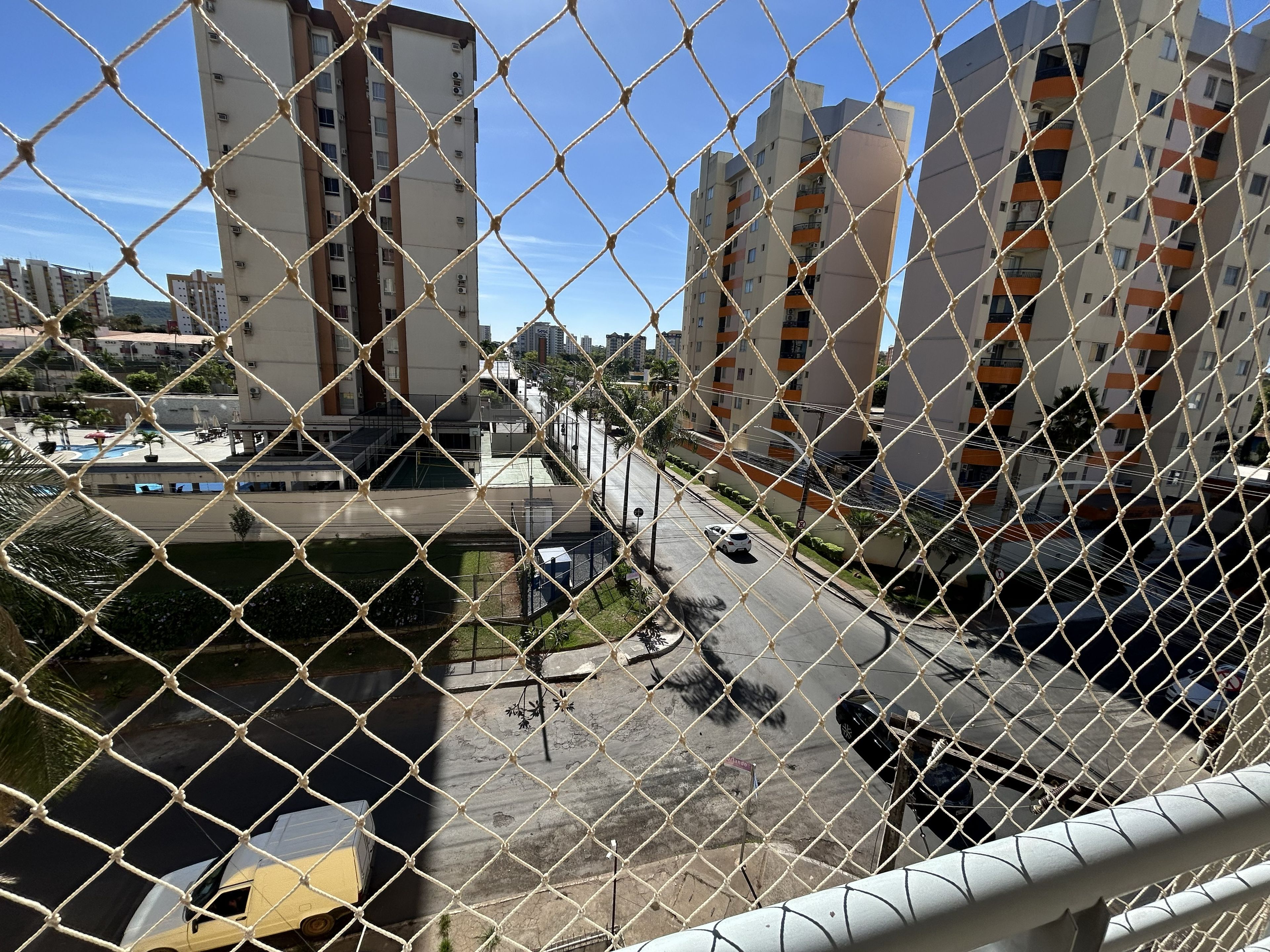 Bairro residencial com edifícios de apartamentos, uma estrada com carros e uma área cercada com piscina.