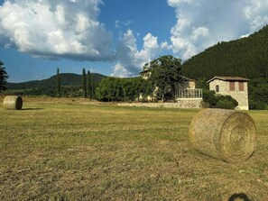 Un paysage rural avec un bâtiment en pierre, des bottes de foin et un ciel dégagé.