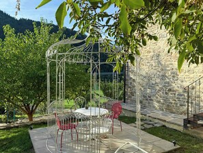 Un belvédère avec une table et des chaises, entouré de verdure et bordé d’un mur de pierre.