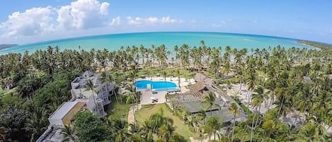 A resort with a swimming pool surrounded by palm trees and a view of the ocean.