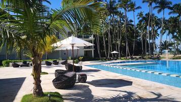 A pool area with lounge chairs, umbrellas, and palm trees.