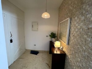 A hallway with a white door, a small potted plant, a wall-mounted light fixture, and a textured wall. - Case Damare Coson bay (Las Terrenas)