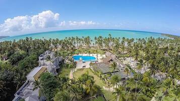 A resort with a swimming pool surrounded by palm trees and a view of the ocean.