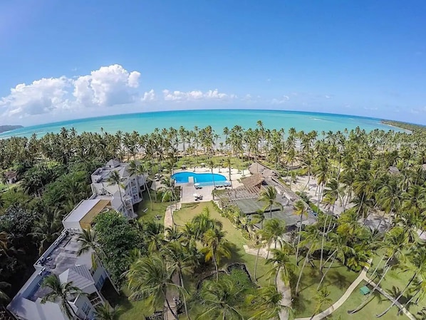 A resort with a swimming pool surrounded by palm trees and a view of the ocean. - Case Damare Coson bay (Las Terrenas)