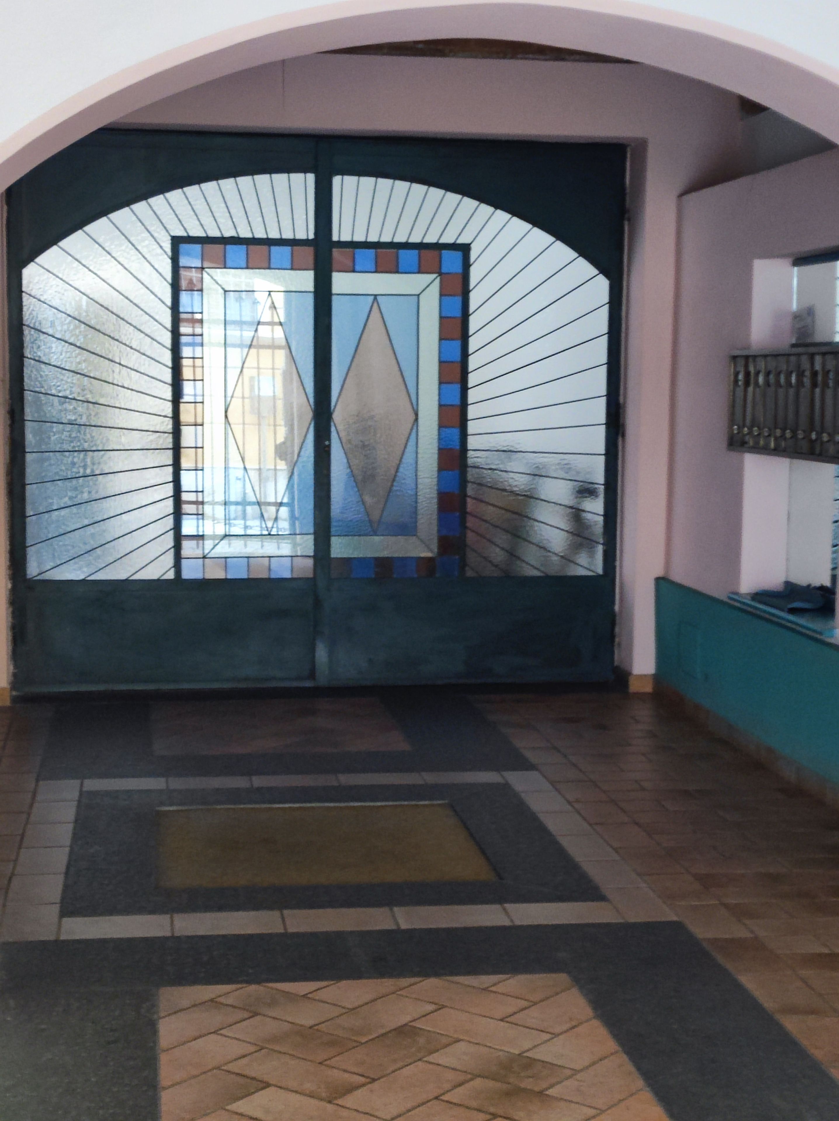 A double door with a geometric stained glass design, leading to a tiled entrance area.