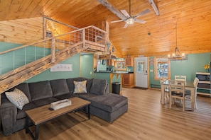 A cozy cabin interior with a wooden staircase, a sofa, a dining table, and a kitchen area. - Secluded Cabin with Hot Tub • Outdoor Shower • Private Trail and Pond (Parrottsville)