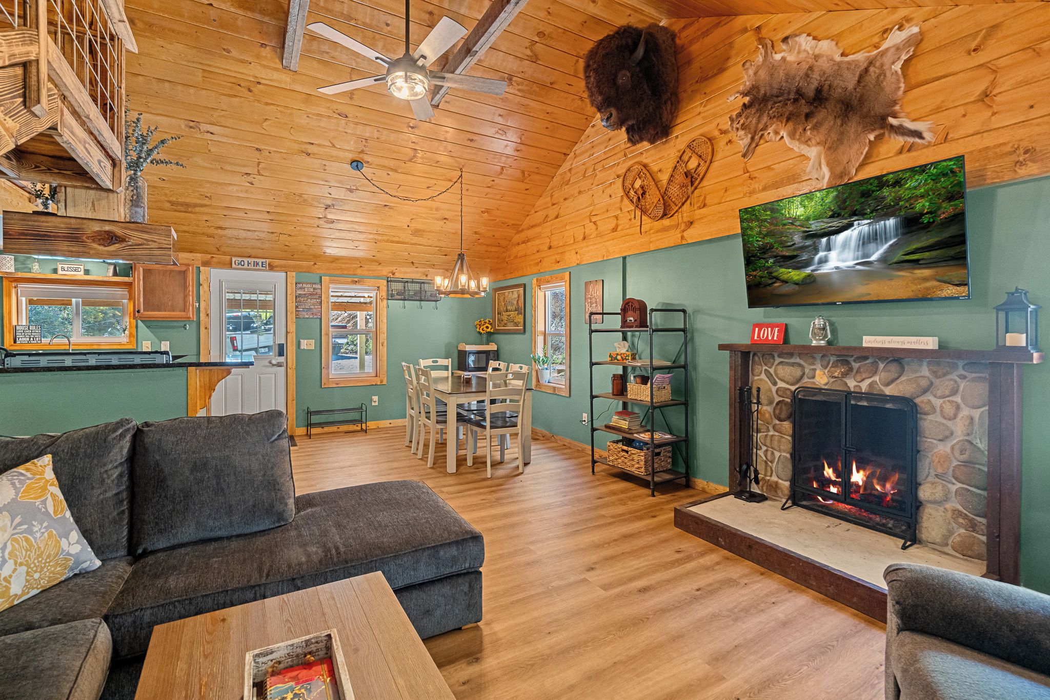 A cozy cabin interior with a fireplace, wooden floors, a dining area, and a television mounted on the wall.