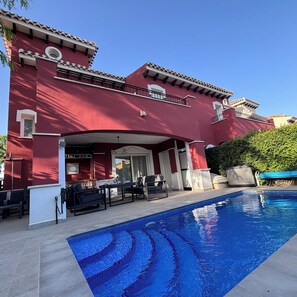 A red building with a pool, outdoor seating, and a covered patio area.