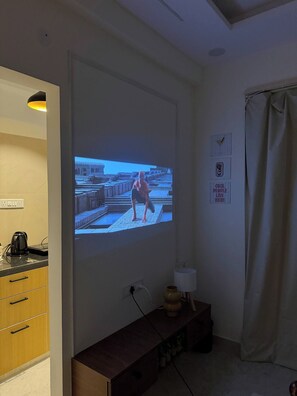 Ein Raum mit an der Wand montiertem Projektor, der eine Szene zeigt, einer Kaffeemaschine, einer Lampe und einem Schild an der Wand.