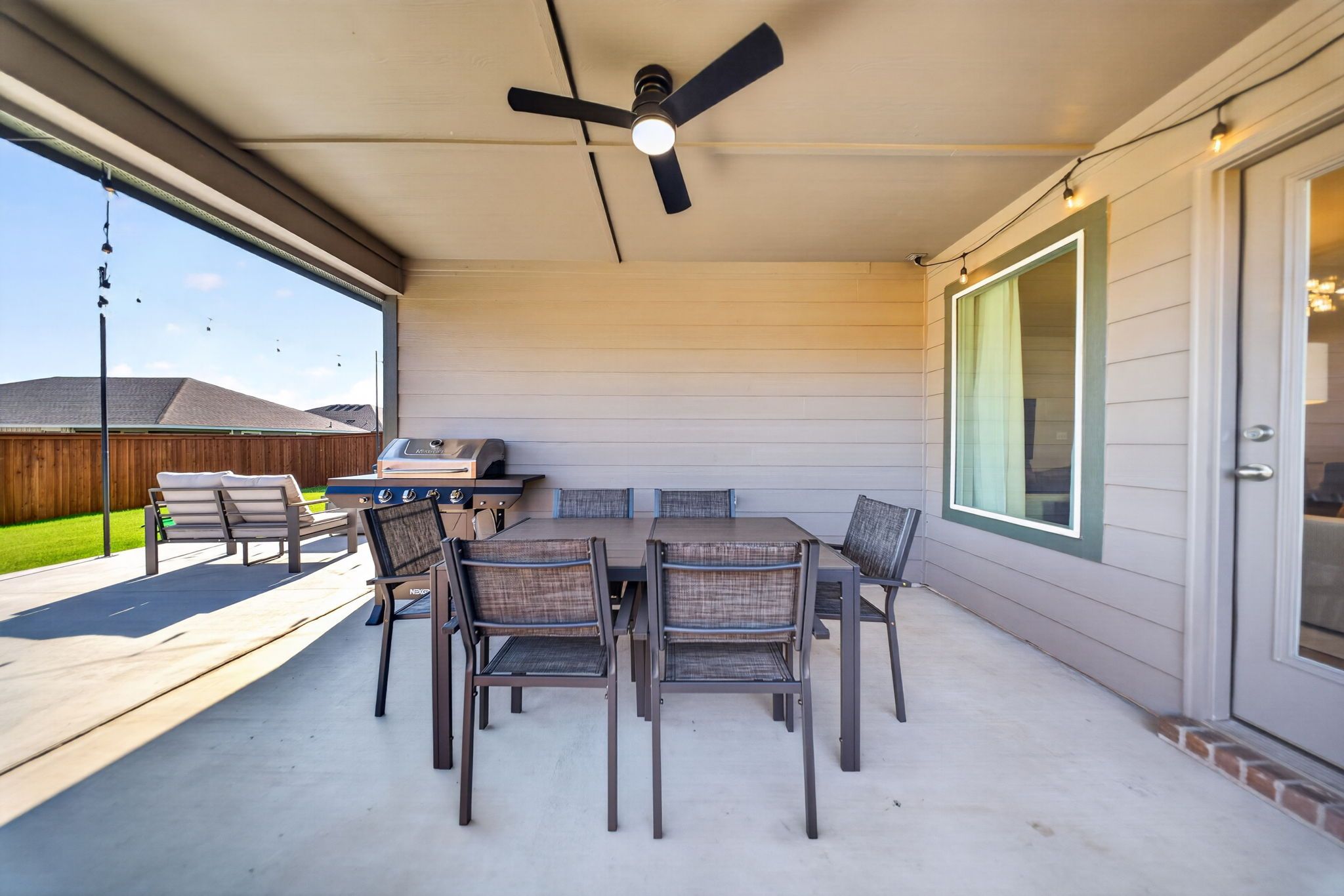 Une terrasse extérieure avec une table et des chaises, un ventilateur de plafond et un barbecue.