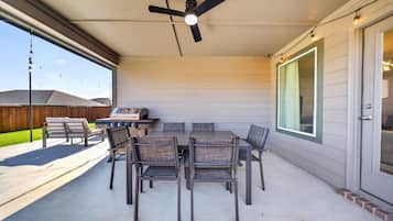 Une terrasse extérieure avec une table et des chaises, un ventilateur de plafond et un barbecue.