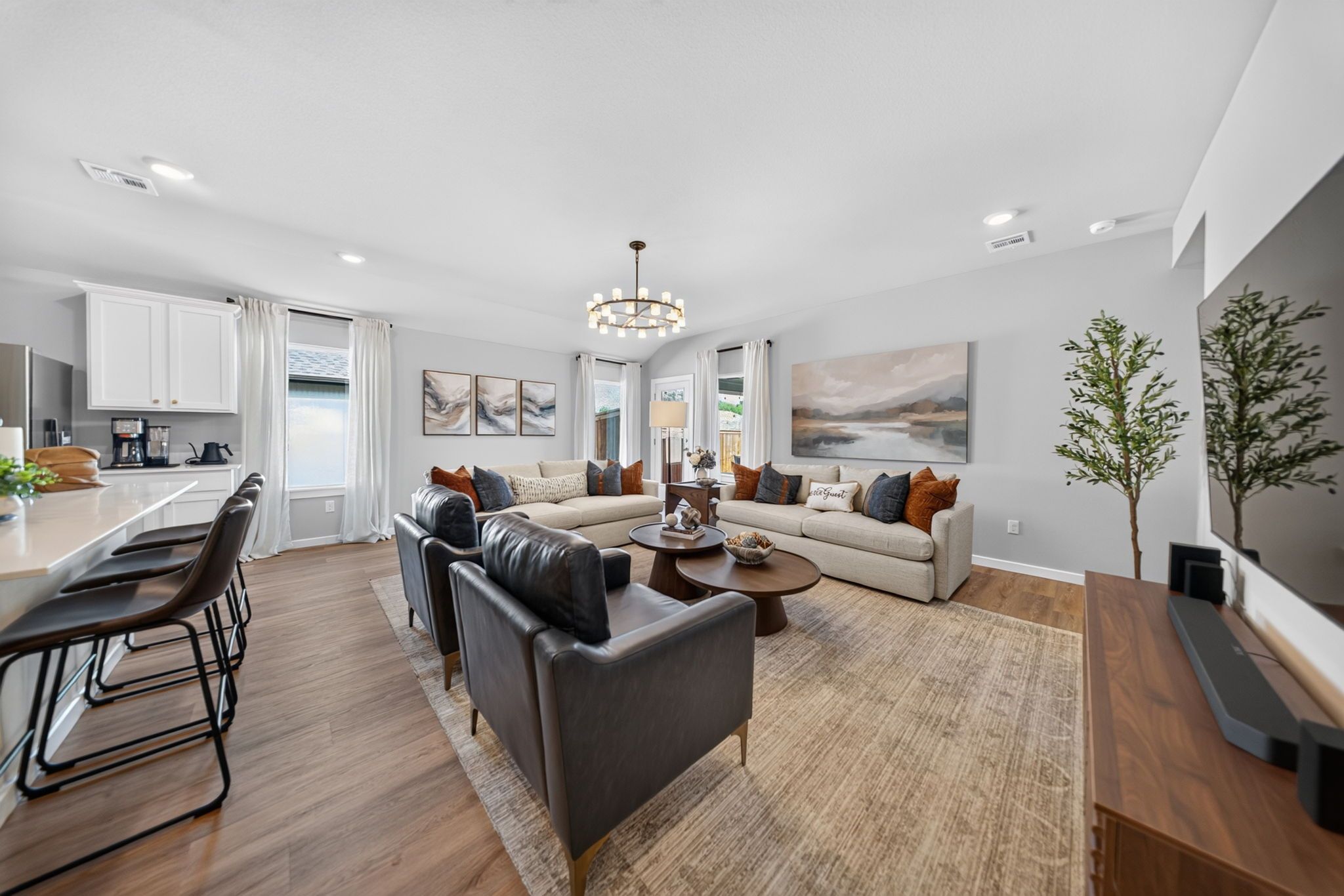 A modern living room with a sofa set, a coffee table, and a dining area with chairs and a kitchen in the background.