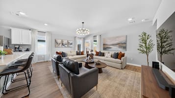A modern living room with a sofa set, a coffee table, and a dining area with chairs and a kitchen in the background.