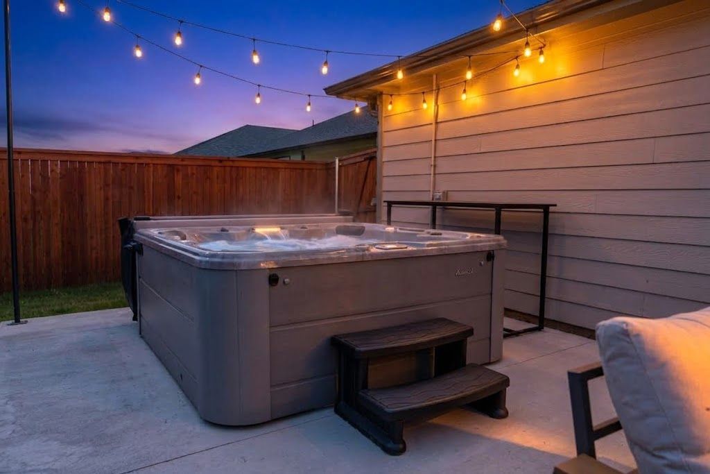 A hot tub with steps, a wooden fence, and string lights in a backyard.