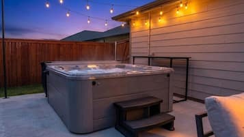 A hot tub with steps, a wooden fence, and string lights in a backyard.
