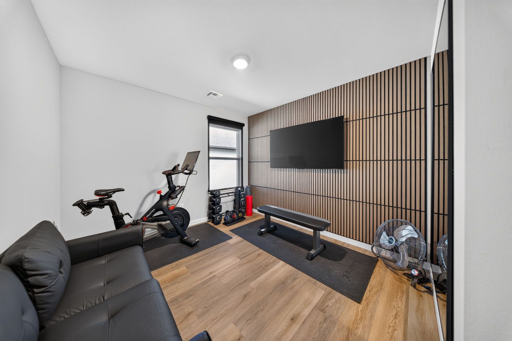 Una sala de estar moderna con un sofá, una bicicleta estática, pesas y un televisor montado en la pared.