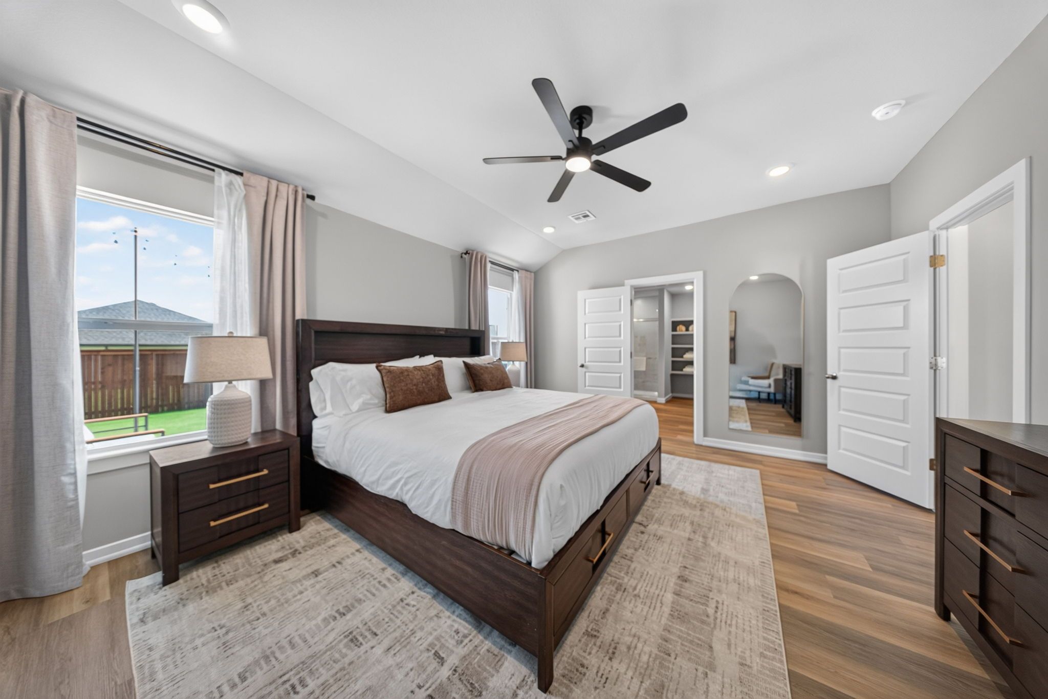 A bedroom with a bed, bedside tables, a ceiling fan, and a view of the outdoors.