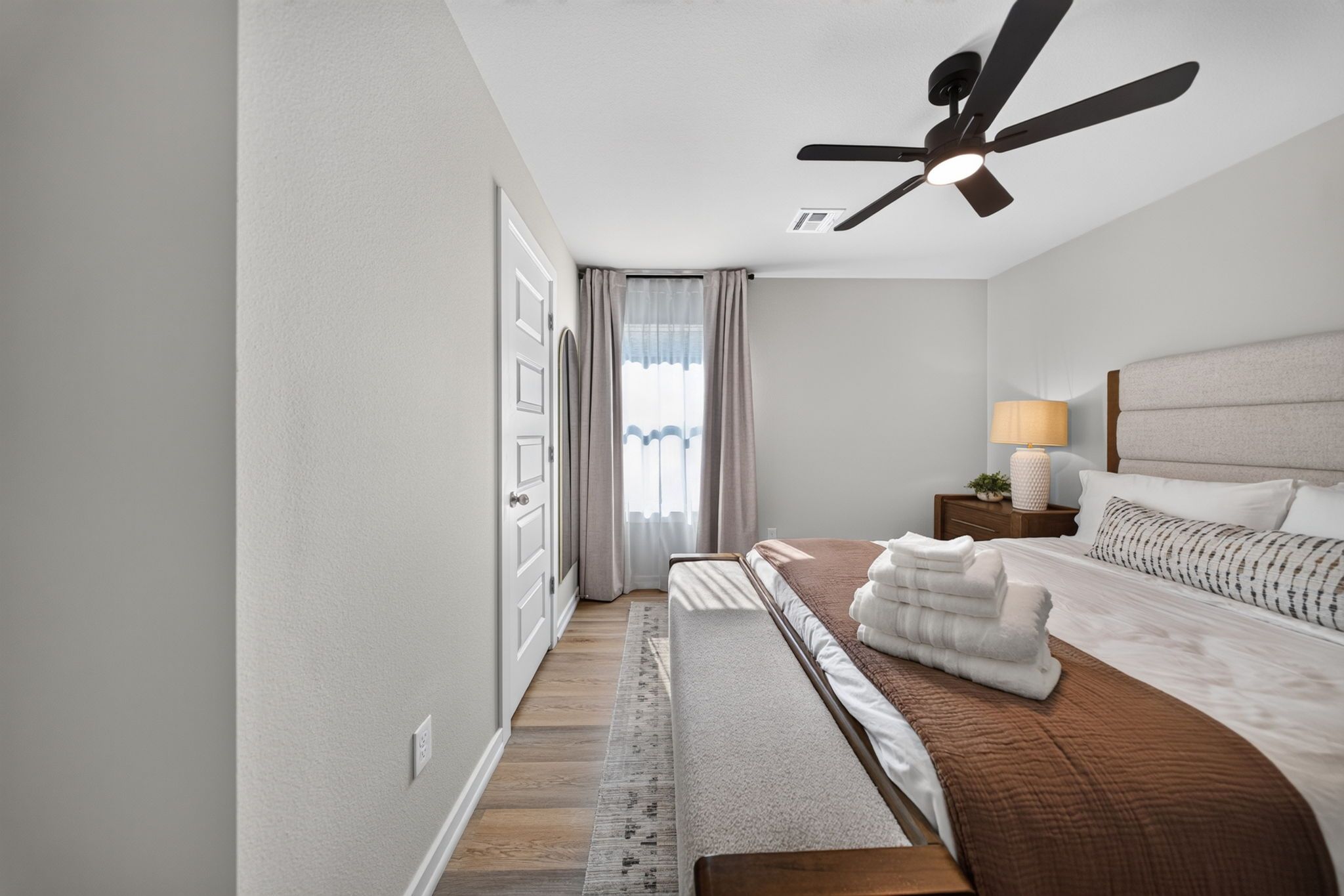 Une chambre à coucher moderne, avec un lit, une table de chevet, une lampe et un ventilateur de plafond.