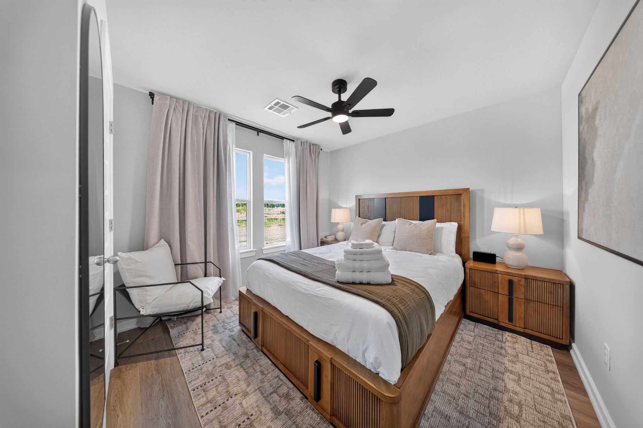 A modern bedroom with a bed, bedside tables, a ceiling fan, and a view of the outdoors.