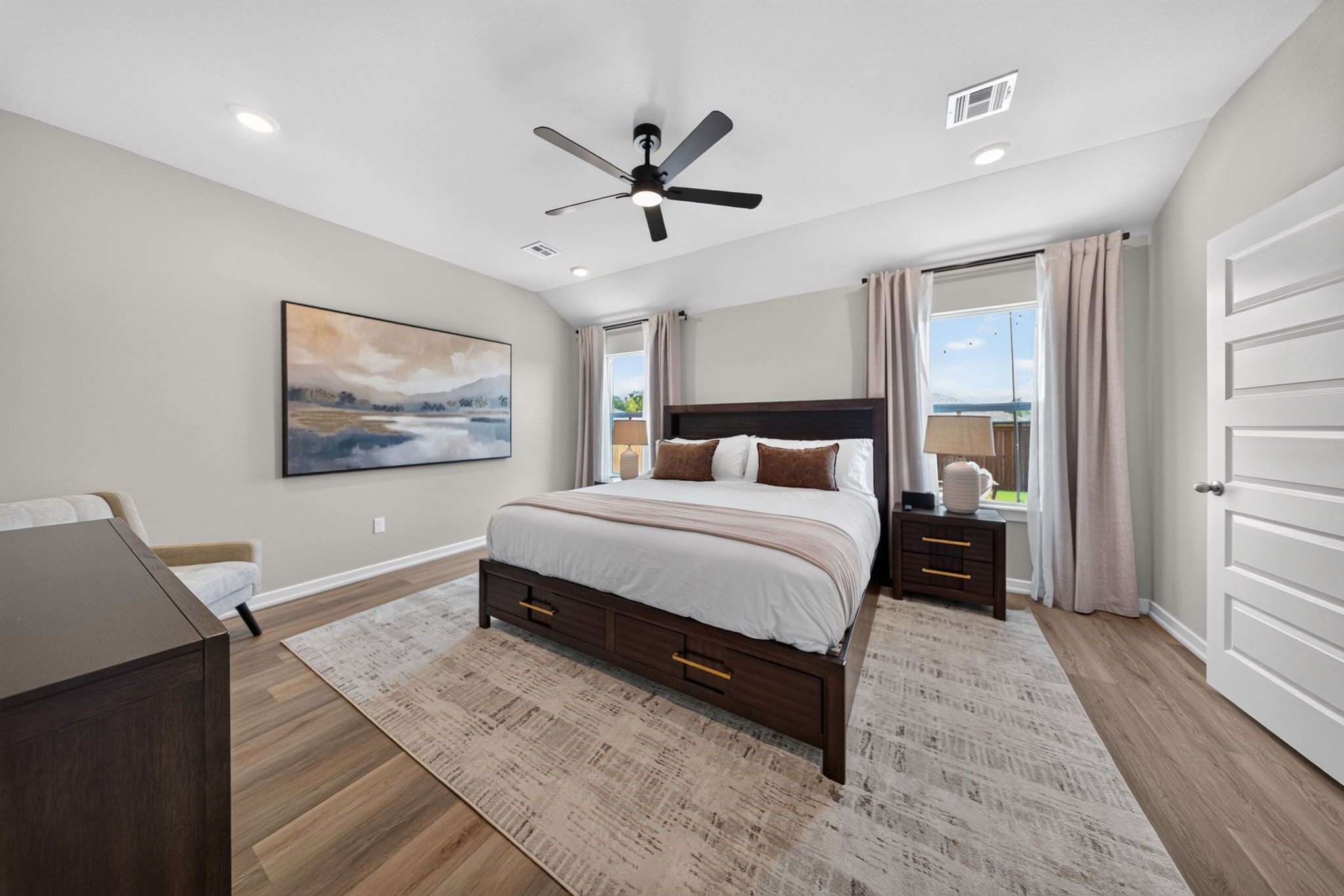 A bedroom with a bed, a nightstand, a desk, a ceiling fan, and a large window with curtains.