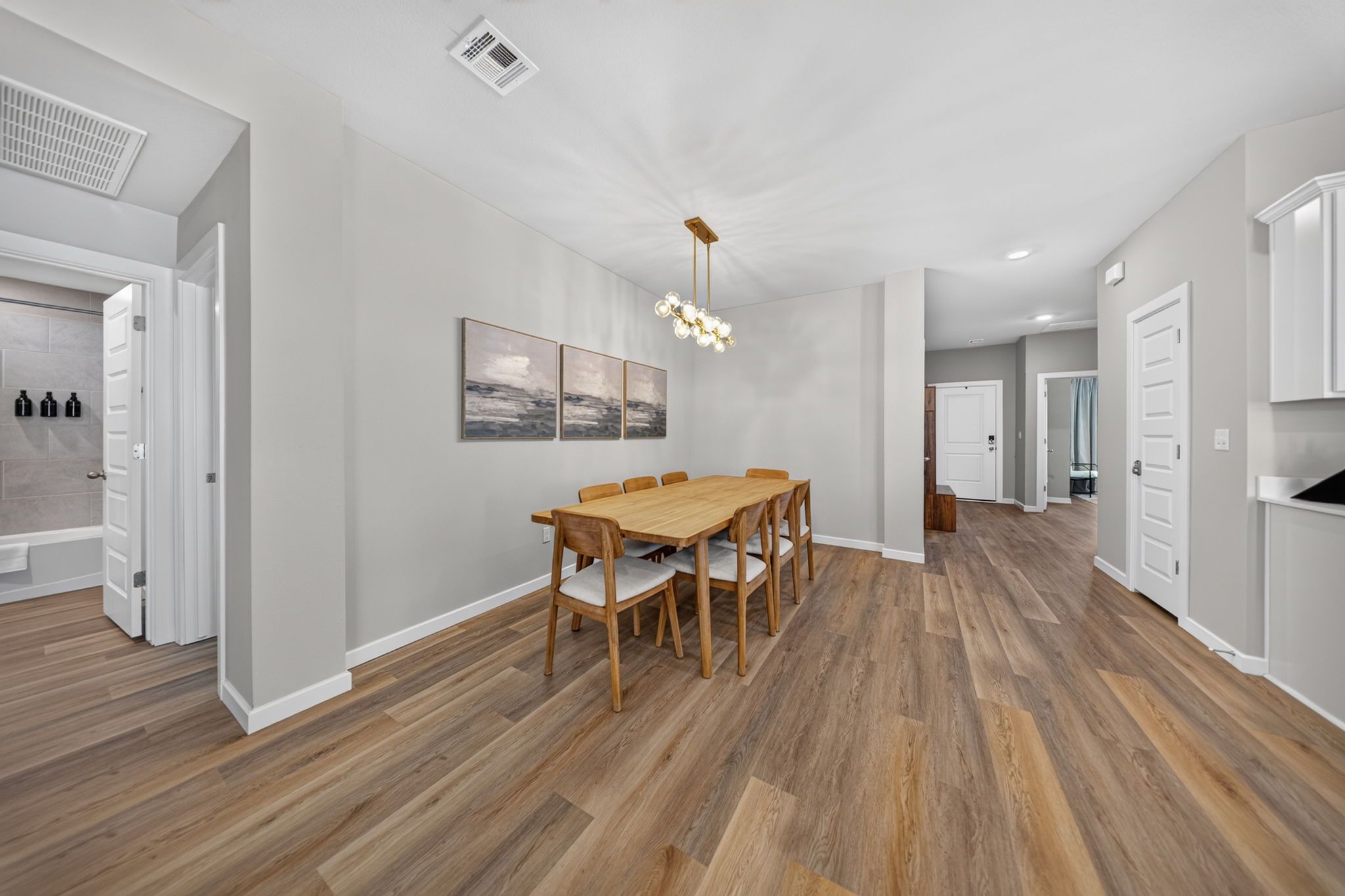 A spacious kitchen with a wooden dining table and chairs, a modern pendant light, and a view into the adjacent living area.