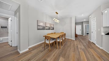 A spacious kitchen with a wooden dining table and chairs, a modern pendant light, and a view into the adjacent living area.
