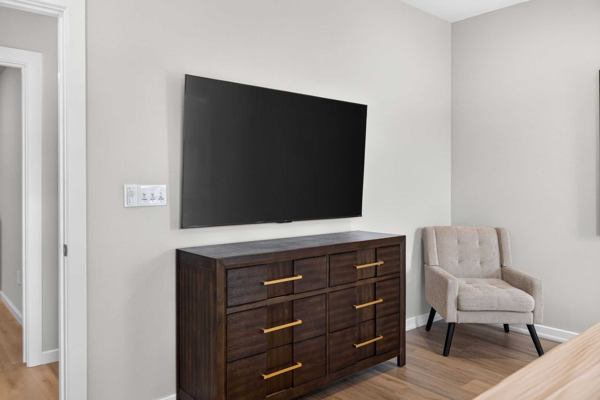 Ein Zimmer mit einem dunklen Holzschrank, einem beigen Sessel und einem großen, schwarzen Flachbildfernseher an der Wand.