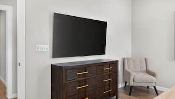 A room with a dark wooden cabinet, a beige armchair, and a large black flat-screen TV mounted on the wall.