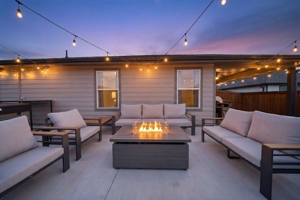 An outdoor seating area with a fire feature, string lights, and a view of the house.