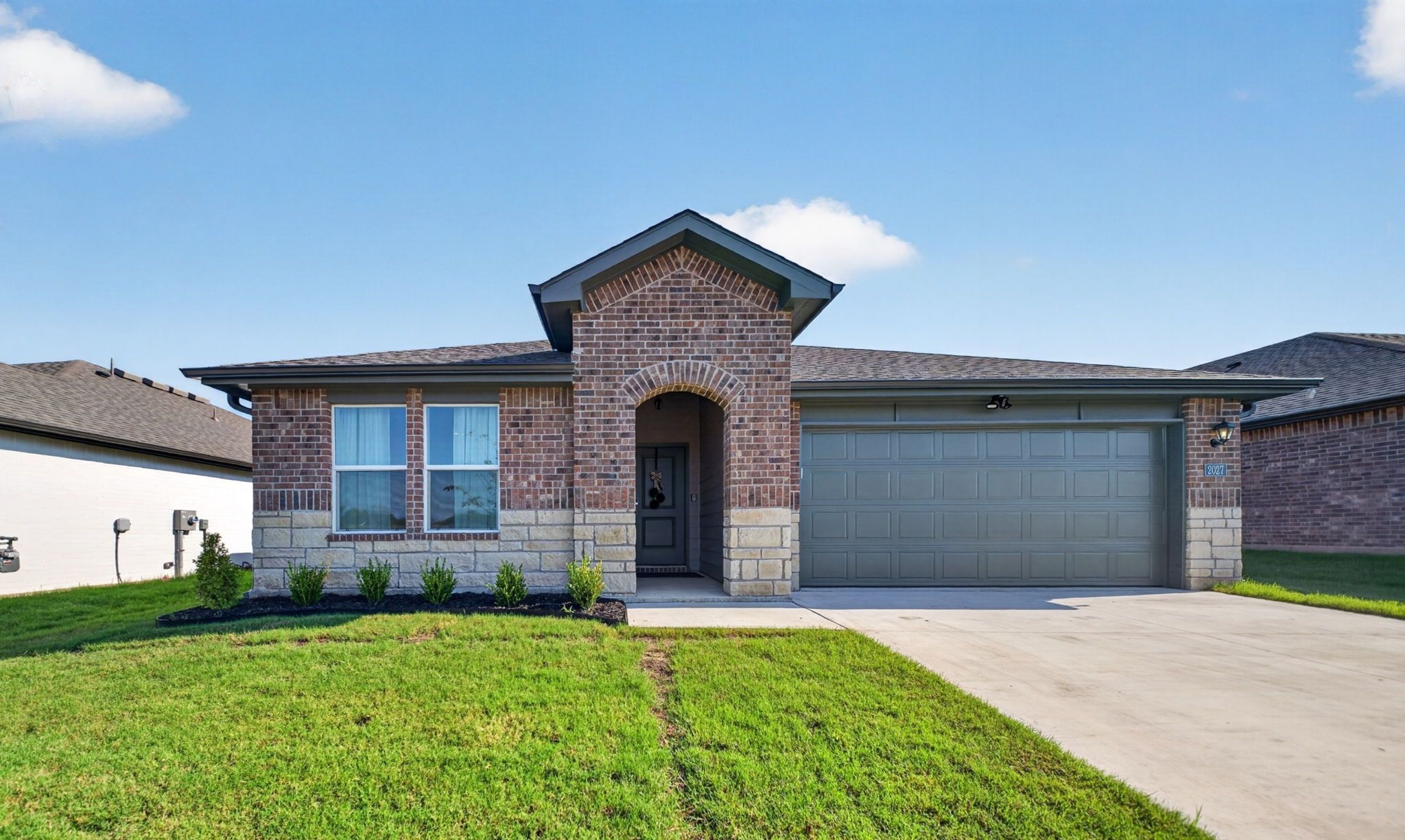 A residential house with a brick facade, a garage, and a well-maintained lawn.