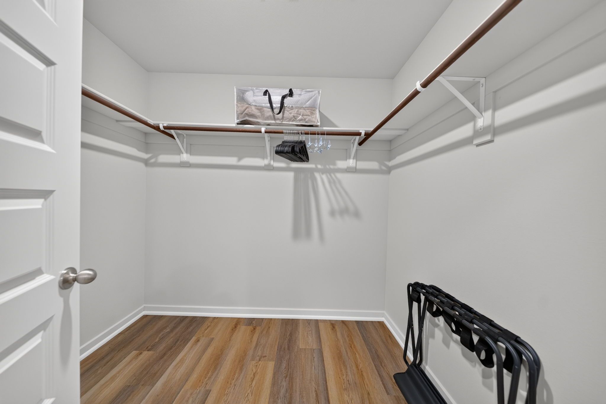 A room with a wooden floor, white walls, a door, and a clothes rack with hanging items.