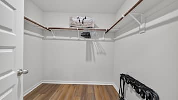 A room with a wooden floor, white walls, a door, and a clothes rack with hanging items.