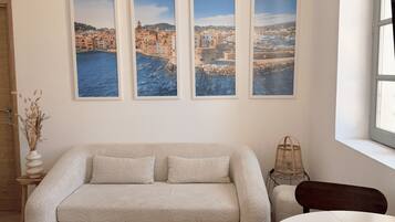 Una sala de estar con un sofá color beige, una mesa redonda blanca y tres fotografías enmarcadas de paisajes costeros en la pared.