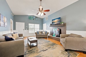 A living room with a ceiling fan, a fireplace, and a large painting on the wall.