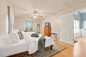 Un dormitorio con una cama, un ventilador de techo, un aparador de madera y una puerta que da a otra habitación.